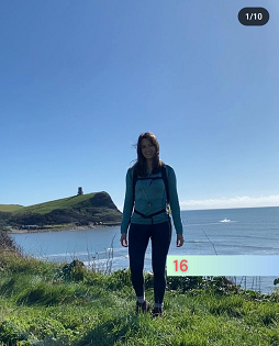 A white female with long brown hair smiles at the camera on a coastal path at Kimmeridge Bay